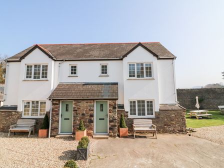 Two story semi detached house with stone and white exterior green doors two benches and potted plants in front at Kingfisher Cottage in Ilfracombe