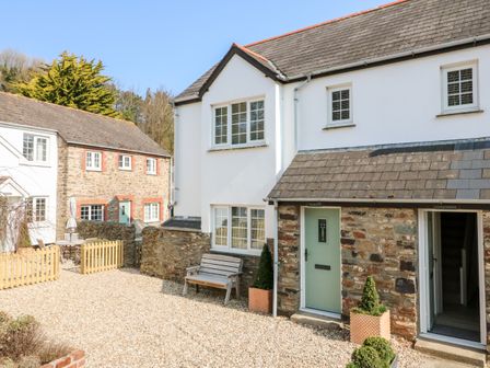 Exterior view of stone and white houses with a gravel courtyard and wooden bench at Heron Cottage in Ilfracombe