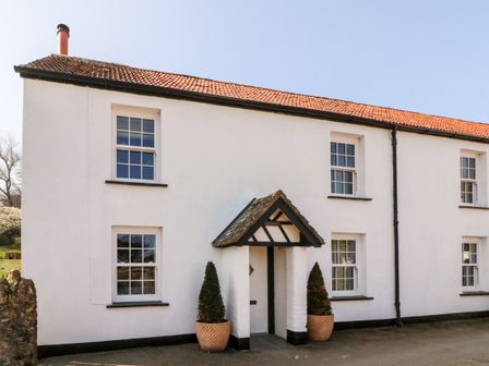 A white two-story cottage with a tiled roof and a porch with potted plants at Pheasant Cottage in Ilfracombe