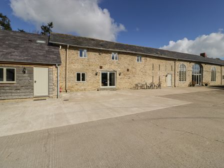 An exterior view of a long stone and wood building with multiple windows and doors and outdoor metal tables and chairs at Timber Barn in Eardisland
