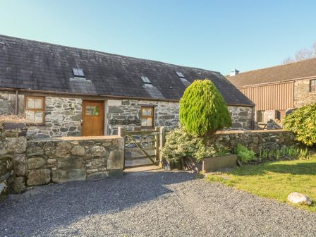 Stone building with wooden door and windows a small gate a gravel driveway a tree and bushes at Beudy Bach in Y Felinheli