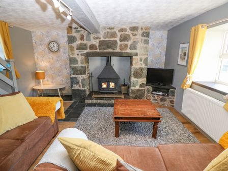 A living room with a stone fireplace wood stove wooden coffee table sofas and yellow curtains at Hendre in Y Felinheli