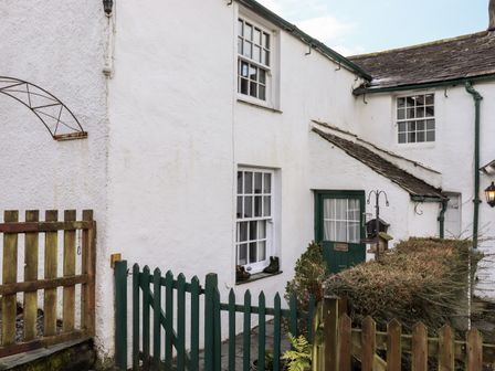 A white exterior wall of a house with green wooden gates and windows at Castle Lodge in Borrowdale
