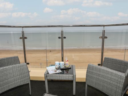 A balcony with two chairs a small table two mugs and a magazine overlooking a sandy beach and ocean at Dolphin View in Rhos-on-sea