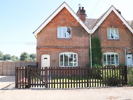 A brick semi detached house with white doors and windows behind a wooden fence at New Park Farm Cottage in Brockenhurst