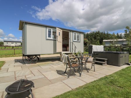 A small mobile cabin with an open door on a patio with chairs a table a fire pit and a hot tub at Shepherd's View in Rhayader