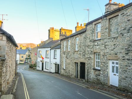 A narrow street with stone and white houses and flags hanging outside at Cosy Cottage in Kirkby Lonsdale