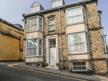 A brick building with bay windows a white front door and two potted plants on a sloped street at Flat 4 in Whitby