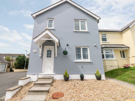 A front view of a grey house with a white door and three potted plants at Sandy Bay House in Saundersfoot