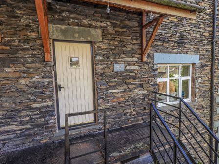 An exterior stone wall with a cream door and window next to a black metal staircase at Loughrigg View in Ambleside