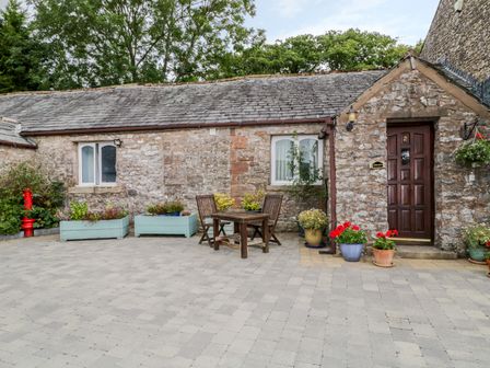 A stone cottage exterior with wooden door and windows and outdoor table and chairs with plants at Rosegarth Cottage in Newby