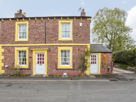A brick house with yellow window and door frames and two white doors on a street at Rose Cottage in Crosby on Eden near Carlisle