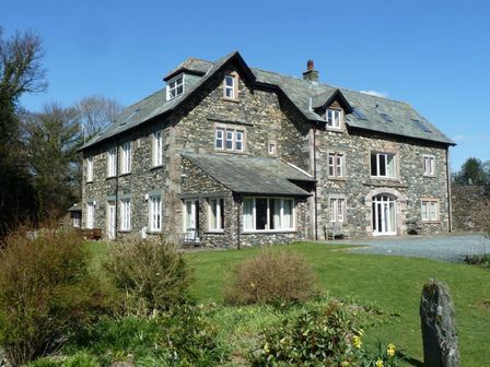 A stone house with multiple windows and a grassy garden in front at Maple Cottage in Keswick