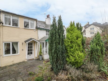 A house entrance with a paved walkway and tall evergreen shrubs in front at Derwent Edge in Portinscale