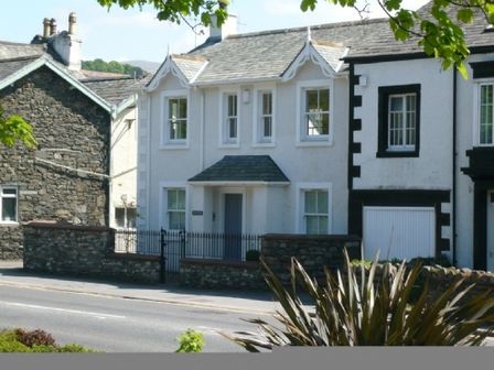 A street view of a white two story house with a stone wall and gate in front at Wrenville in Keswick