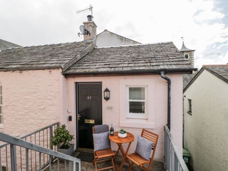 A small exterior area with a black door numbered 27 a window and a wooden table with two chairs at The Old Hayloft in Keswick