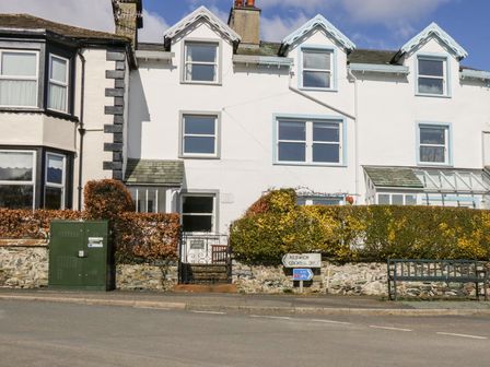 A street view of white terraced houses with hedges a green utility box a bench and street signs at Prospect Lodge in Portinscale