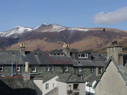 Rooftops of stone and slate houses with chimneys and hills with patches of snow in the background at Helvellyn in Keswick