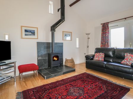 A living room with a wood-burning stove a black leather sofa and a red patterned rug at Esthers Barn in Cockermouth