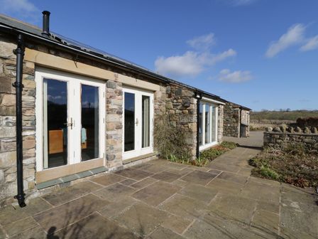 A stone exterior of a house with white framed glass doors and a paved patio area at Buttermere in Cockermouth
