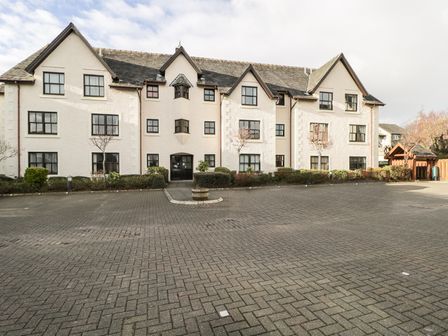 A paved parking area in front of a multi-story white building with multiple windows and a central entrance at Andra Ghyll in Keswick