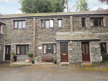 Stone cottages with wooden doors and windows with potted plants and a bench outside Heather Cottage in Ambleside