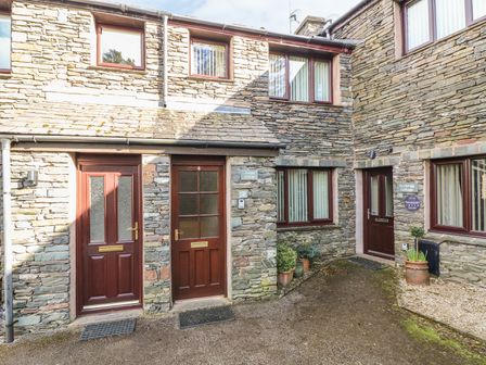 Stone cottages with brown doors and multiple potted plants outside at Juniper Cottage in Ambleside