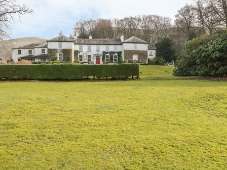 A large white house with a red door behind trimmed hedges and an expansive lawn with trees at Thirlmere Suite in Thirlmere