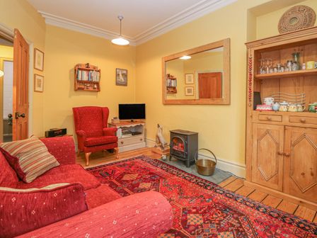 A living room with a red sofa and armchair a wooden cabinet a stove and a large mirror at Tom Heights in Ambleside