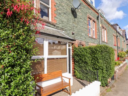 A row of stone houses with a wooden bench and green bushes outside at Archers in Keswick