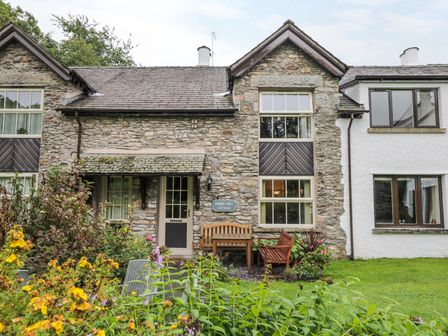Exterior of a stone cottage with a wooden bench and chairs in a garden at Bobbin Mill Cottage in Windermere