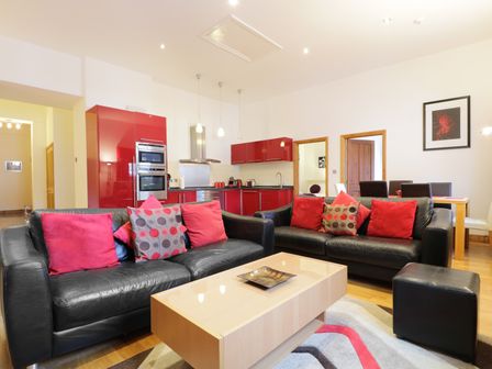A living area with black leather sofas and red cushions a wooden coffee table a kitchen with red cabinets and stainless steel appliances and a dining table with chairs at Keswick Loft in Keswick