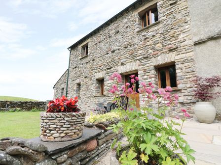 A stone house with wooden windows and a garden with flowers in stone planters at Grayrigg Foot Stable in Grayrigg