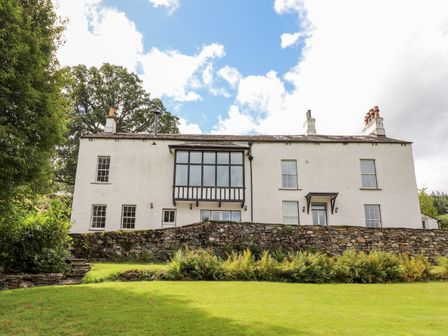 A white two-story house with multiple windows and chimneys a stone wall and green lawn in front at How End in Braithwaite