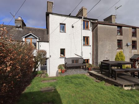 A backyard with a wooden bench and table set on a grassy area at Puddle Duck Cottage in Spark Bridge