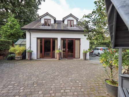 A paved driveway with potted plants outside a two-story white house with two dormer windows and glass doors at Stonegarth Mews in Grasmere