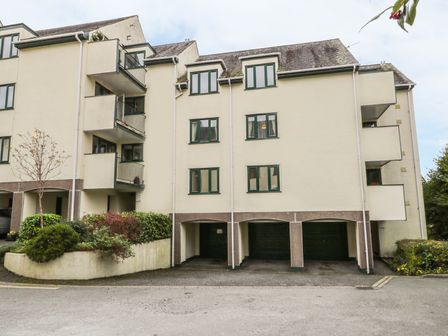 A residential building with balconies and covered parking spaces surrounded by shrubs at Tree Tops View in Bowness-On-Windermere