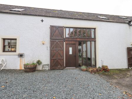 A gravel courtyard with wooden doors and windows on a white building at Tithe Cottage in Cockermouth