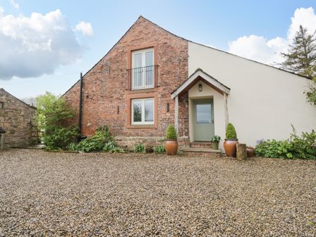 A brick and white exterior cottage with a gravel driveway and potted plants at Stockwell Hall Cottage in Caldbeck