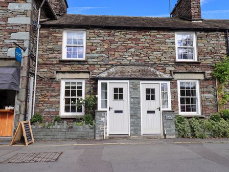 Two white doors and four windows on a stone cottage with plants in front at Beck Steps 1 in Grasmere