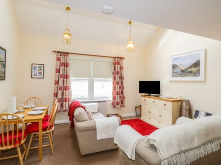A living room with sofas a dining table with chairs a television on a cabinet and patterned curtains at Castlerigg in Keswick