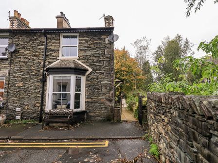 A stone house with a bay window and a bench outside next to a stone wall and a garden gate at Walkers Rest in Windermere