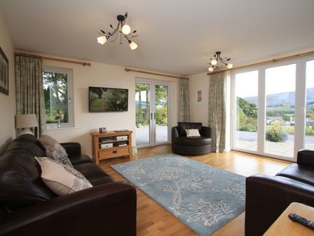 A living room with leather sofas a blue rug and large windows at Eribel Cottage in Threlkeld