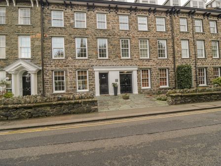 A stone building with multiple windows and black doors along a street with double yellow lines at Derwentwater Apartment Keswick