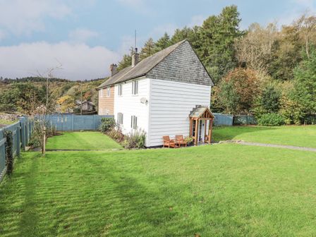 A two-story house with white and brown siding surrounded by a green lawn and trees at Foresters Cottage in Satterthwaite