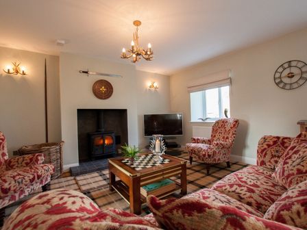 A living room with patterned armchairs and sofa a wood stove a checkered carpet and a chessboard coffee table at Westmains Farm in Penton