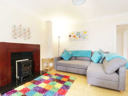 A living room with a grey sofa and blue cushions near a fireplace and colorful rug at Fox's Den in Keswick