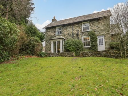 A stone house with shrubs and grass lawn in front at The Old Vicarage in Keswick