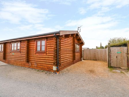 The exterior of a log cabin with windows a gravel area and a wooden fence with gates at Church View in Greetham Rutland