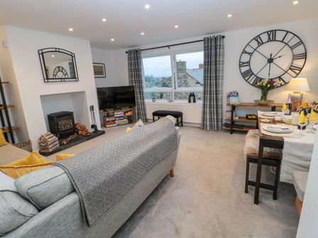 A living room with a sofa fireplace large clock and dining table at Wynding Apartment in Amble-By-The-Sea